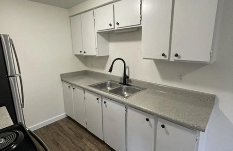 A kitchen with white cabinets and a black refrigerator.